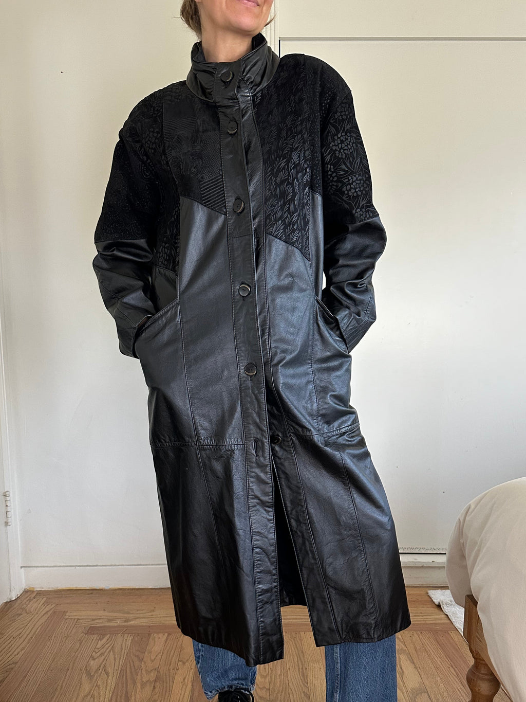 Person wearing a black raincoat indoors on a wooden floor.