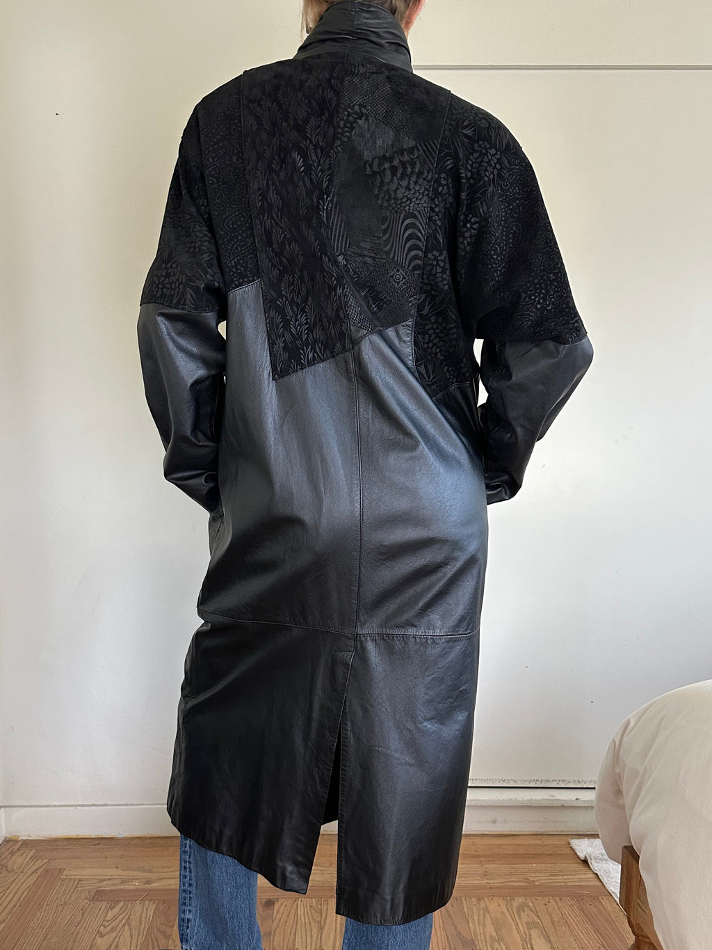 Person wearing a black leather jacket in a room with wooden floor and white walls.