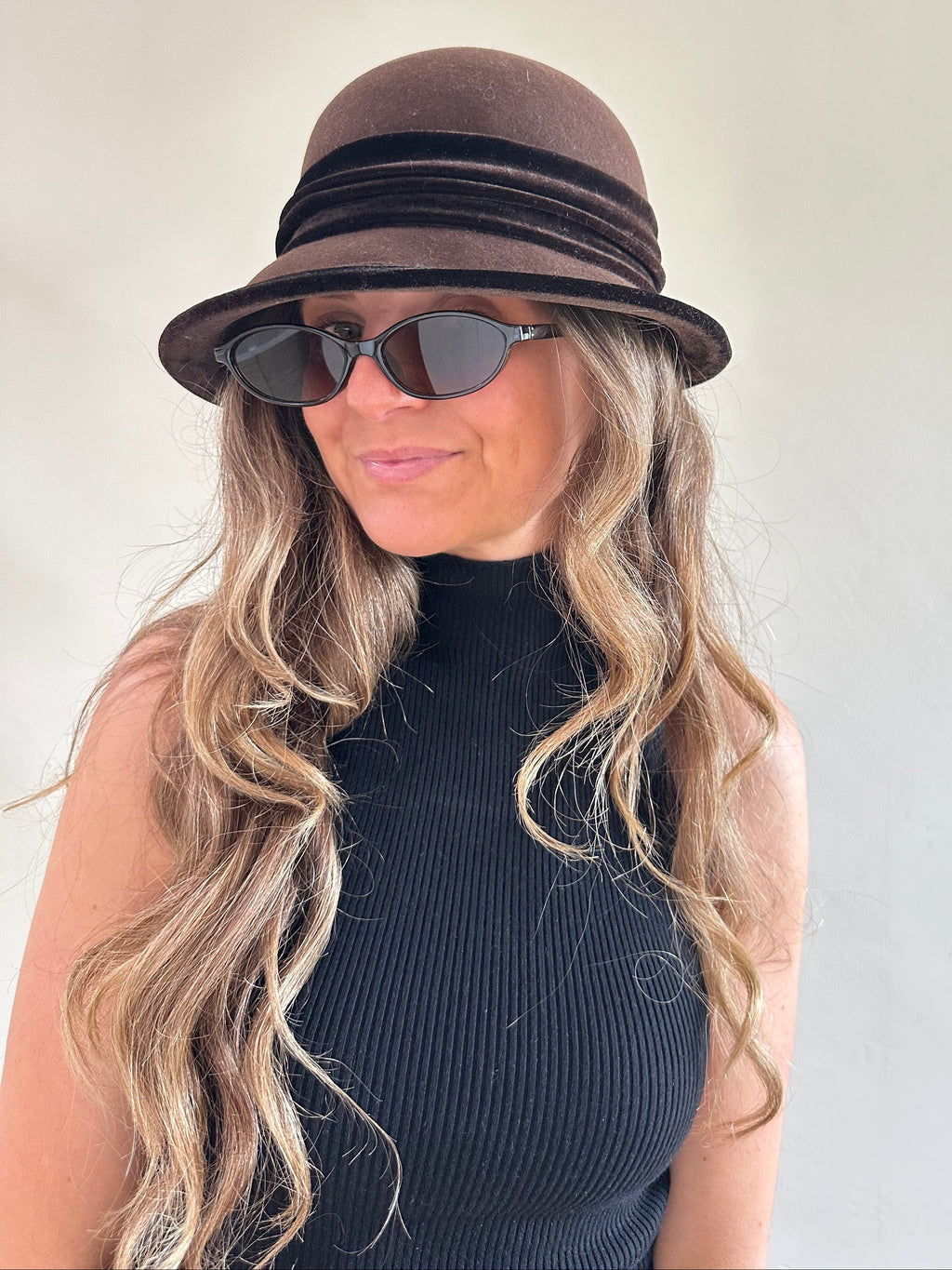 Woman wearing a brown hat and sunglasses with a neutral background