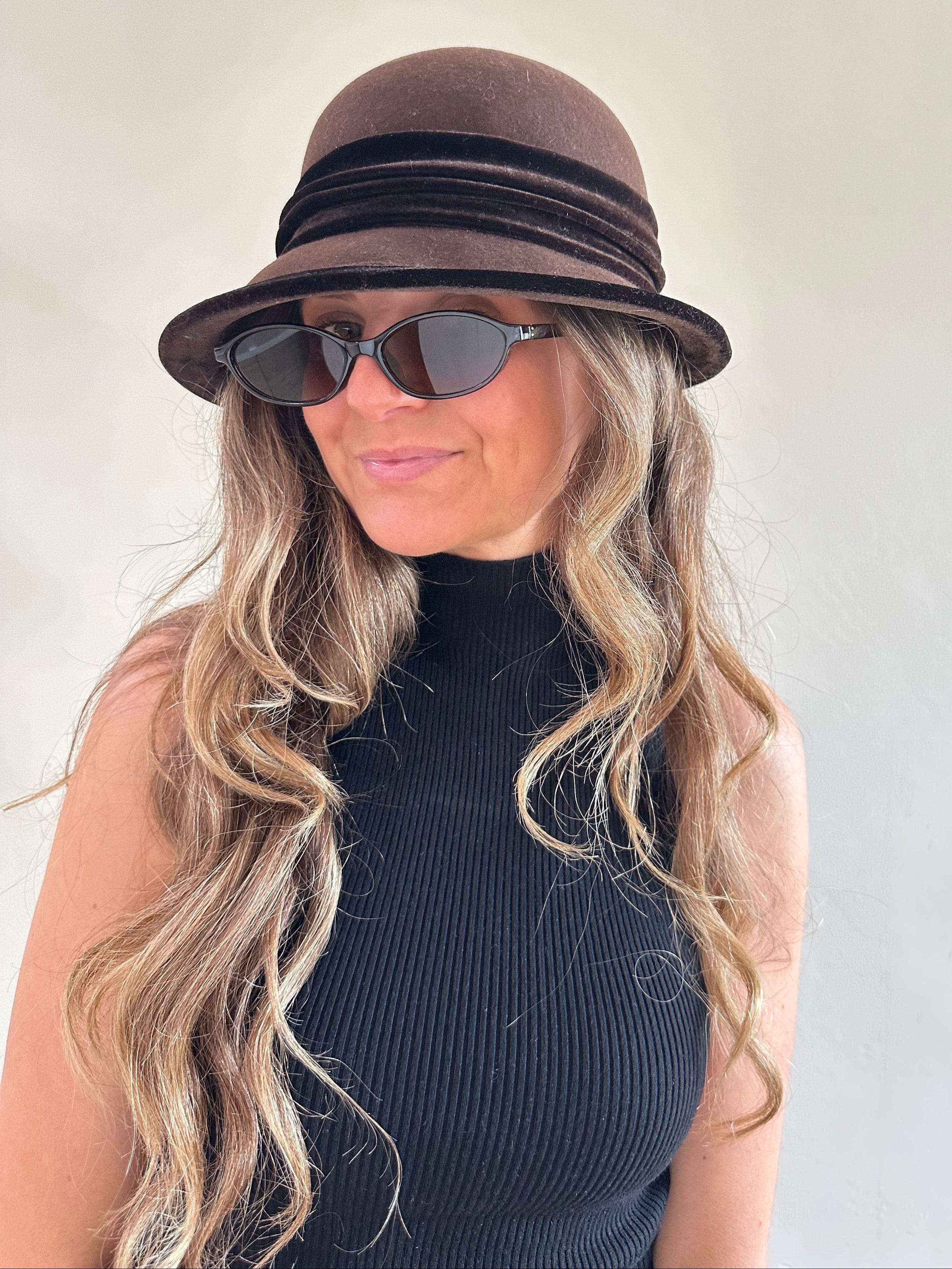 Woman wearing a brown hat and sunglasses with a neutral background