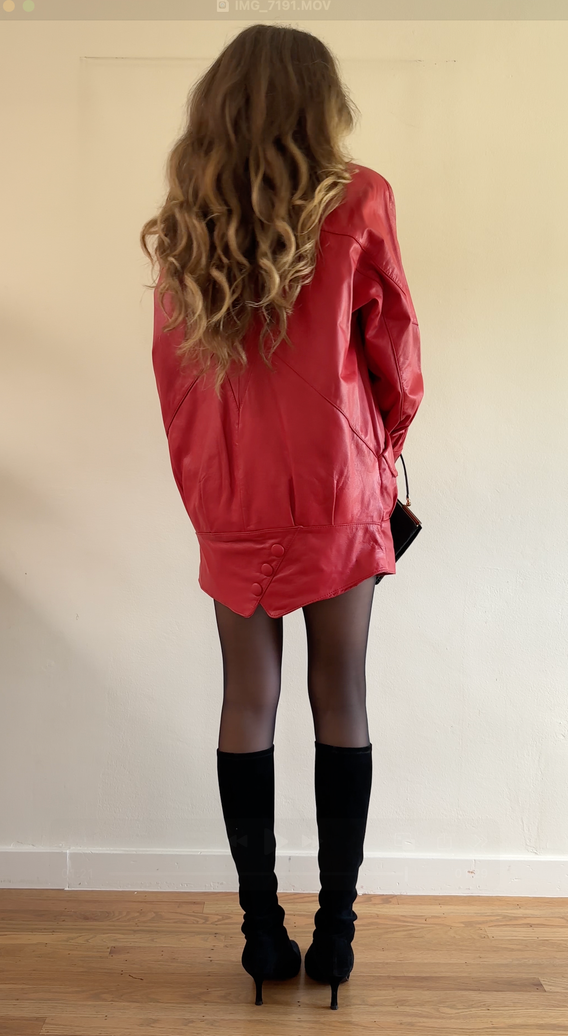 Person wearing a red dress and black knee-high boots standing against a plain wall.