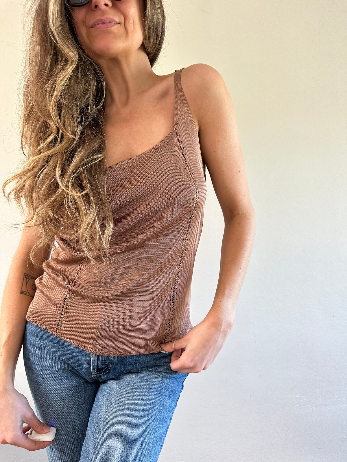 Woman wearing a brown tank top and blue jeans against a plain background