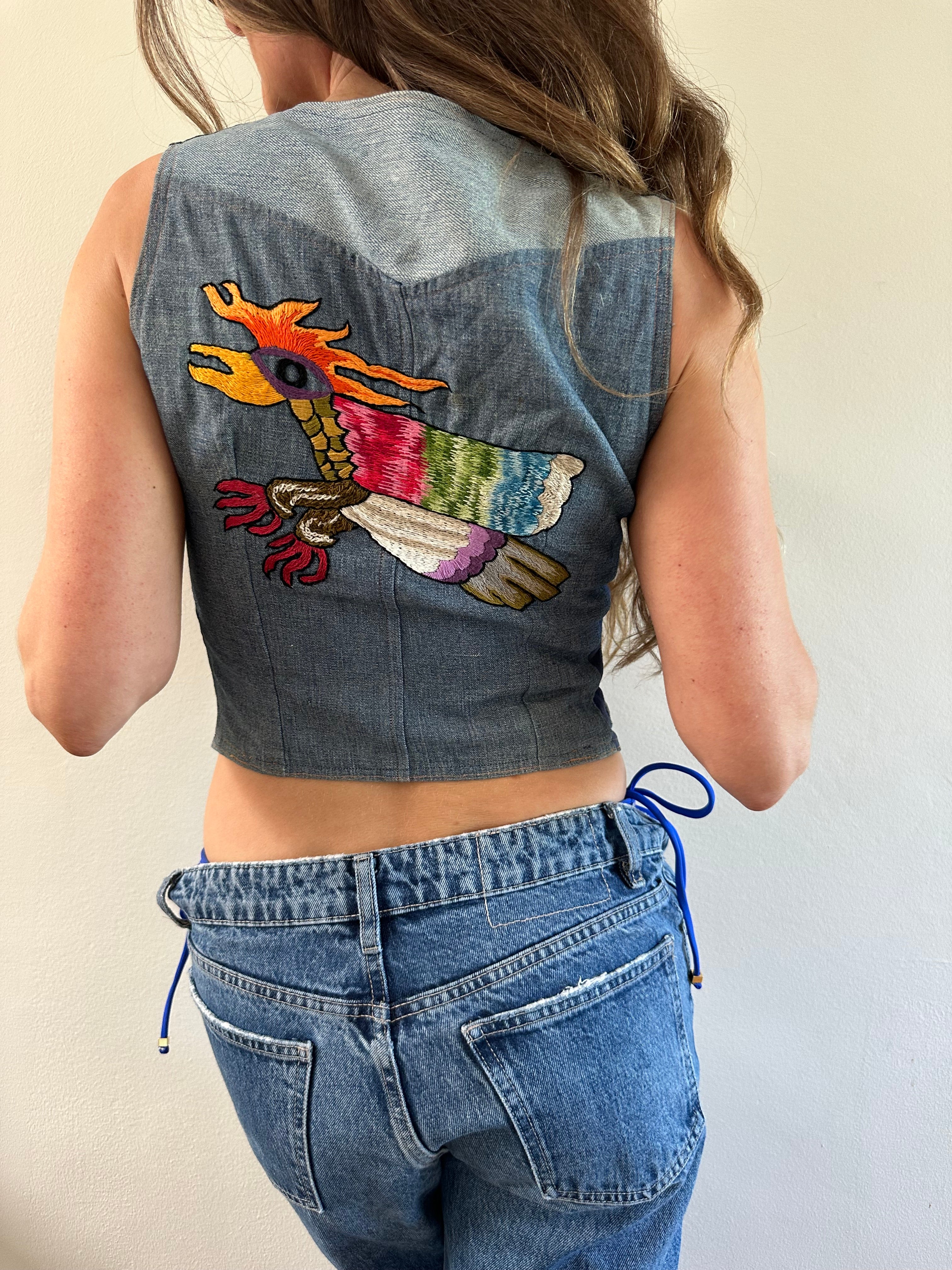 Person wearing a denim shirt with colorful embroidery on a plain background