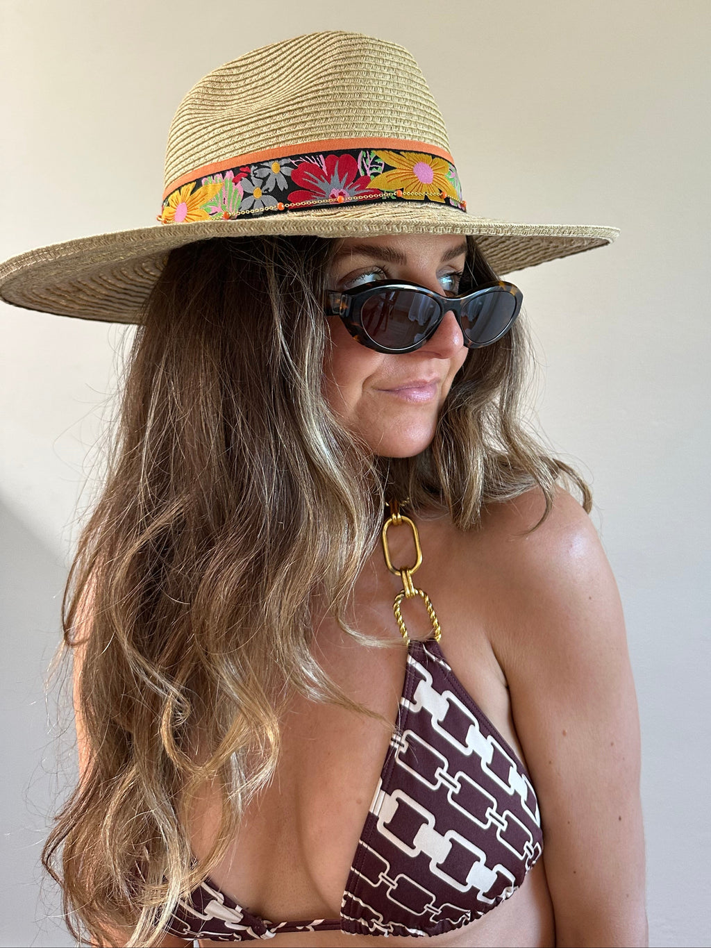 Woman wearing a straw hat with a colorful band and sunglasses, lying on a beach.