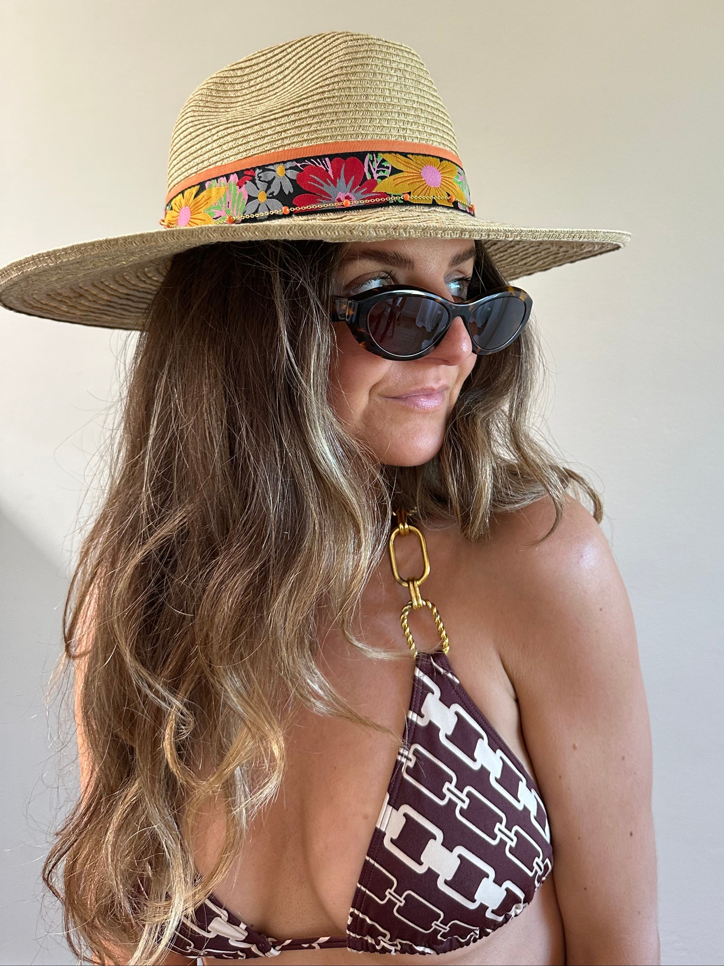 Woman wearing a straw hat with a colorful band and sunglasses, lying on a beach.