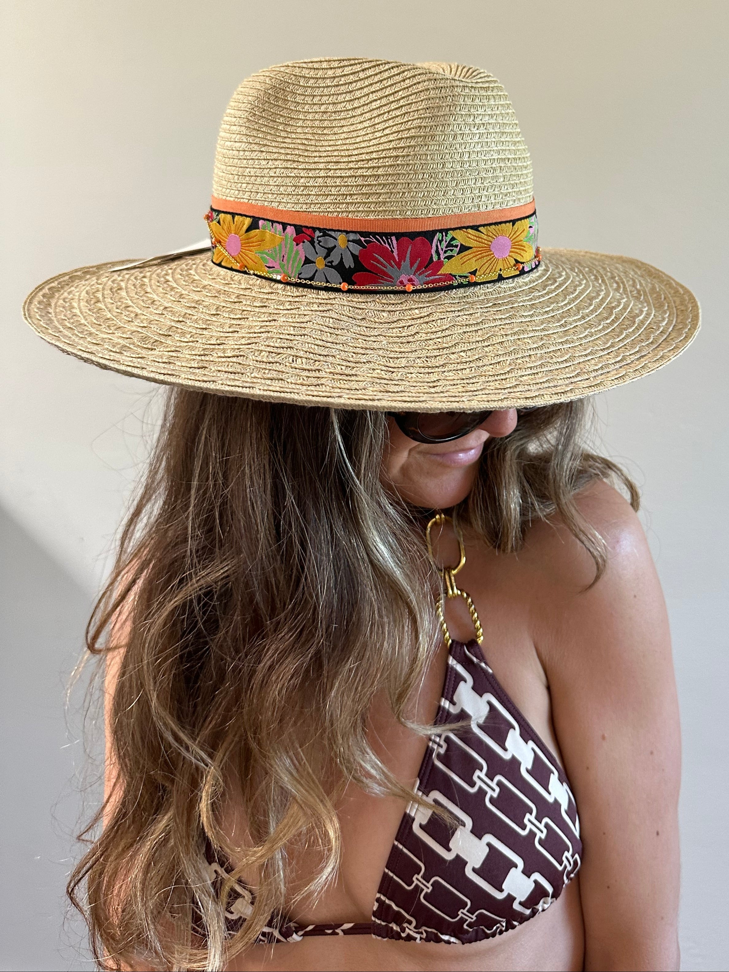 Person wearing a straw hat with a colorful band and a patterned bikini top on a light background