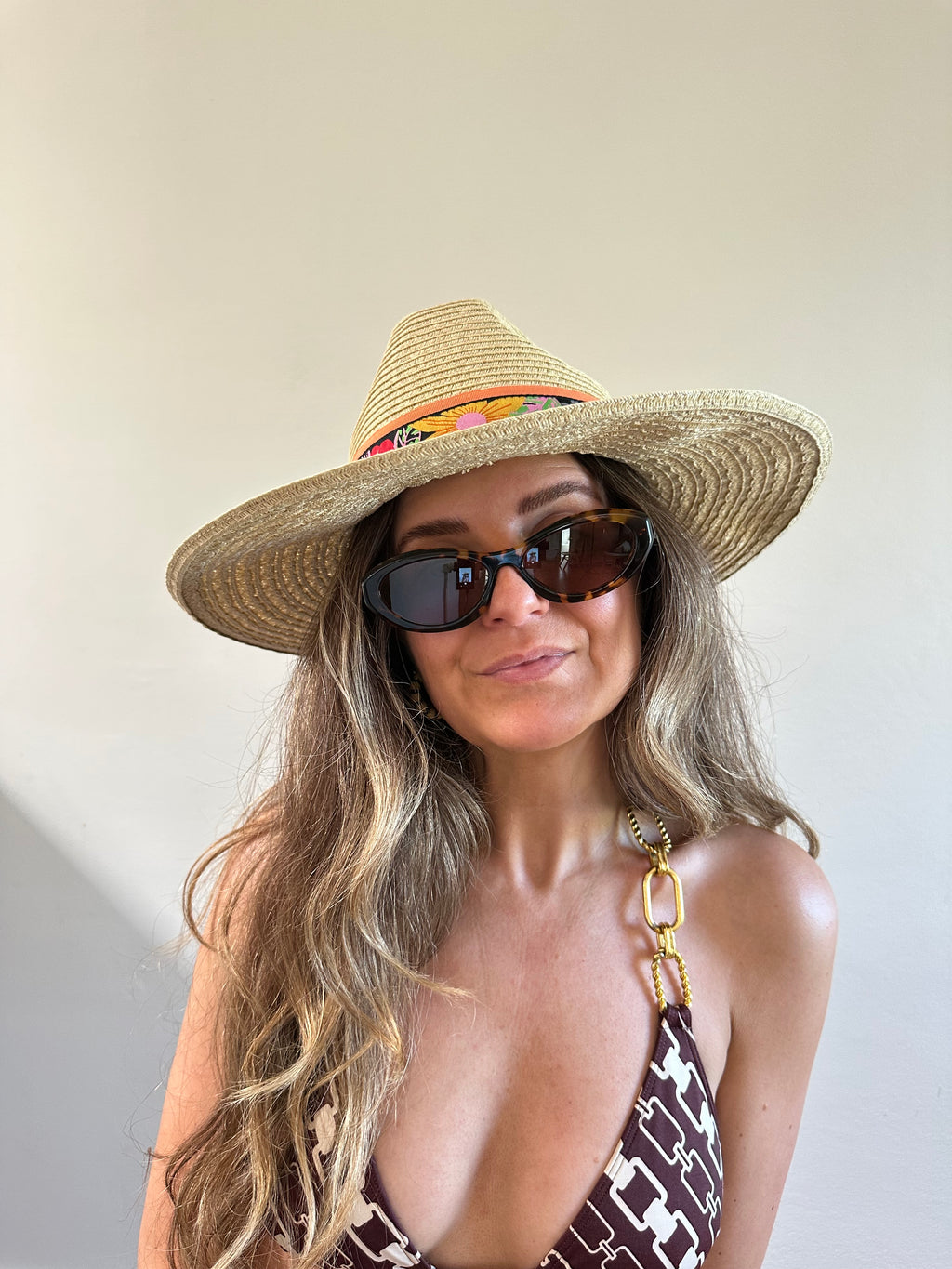 Woman wearing a straw hat and sunglasses with a neutral background
