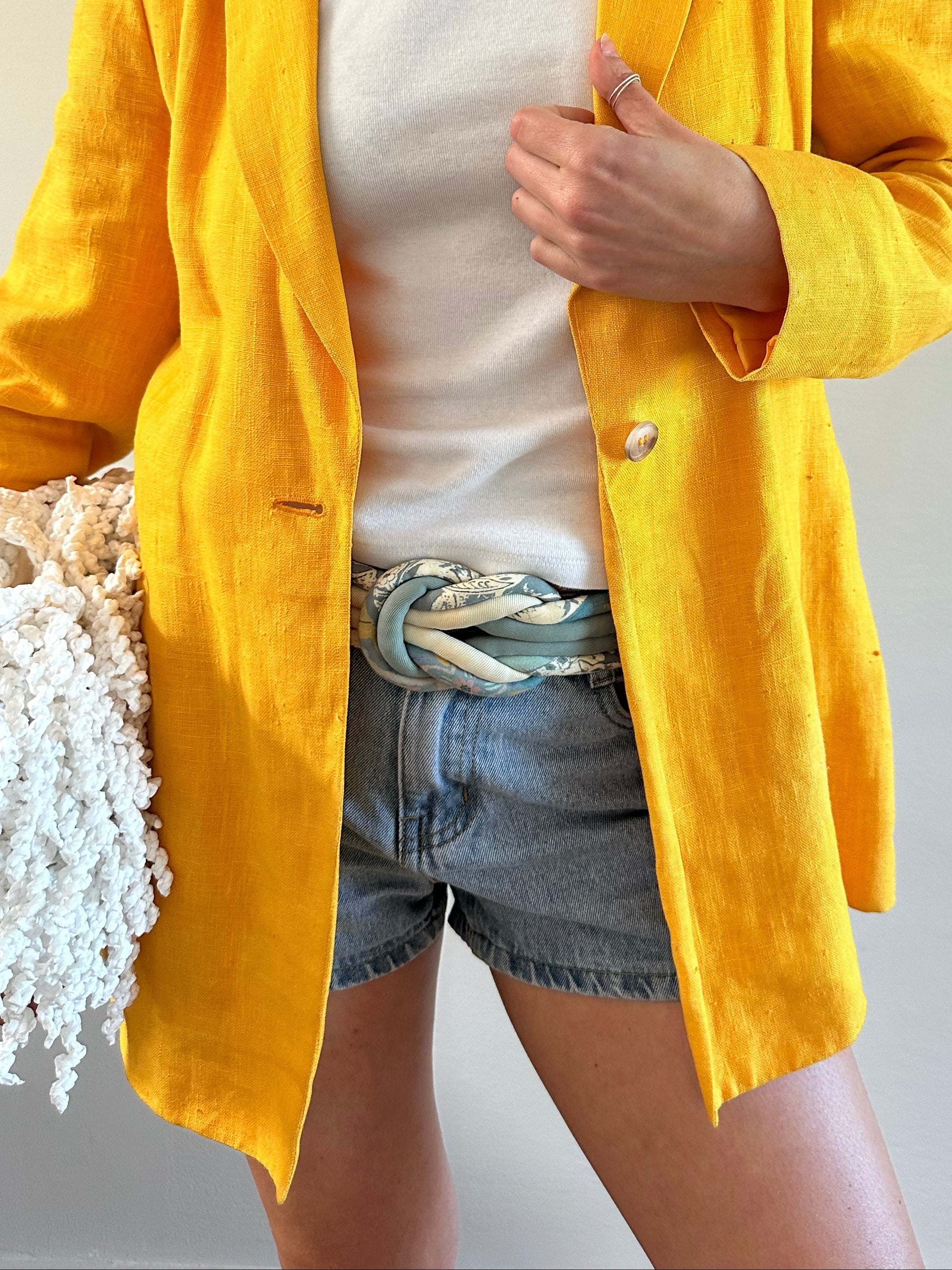 Person wearing a yellow blazer and a vintage belt with a plain background