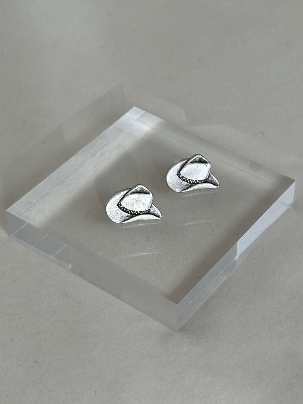 Silver cowboy hat earrings on a clear stand against a gray background