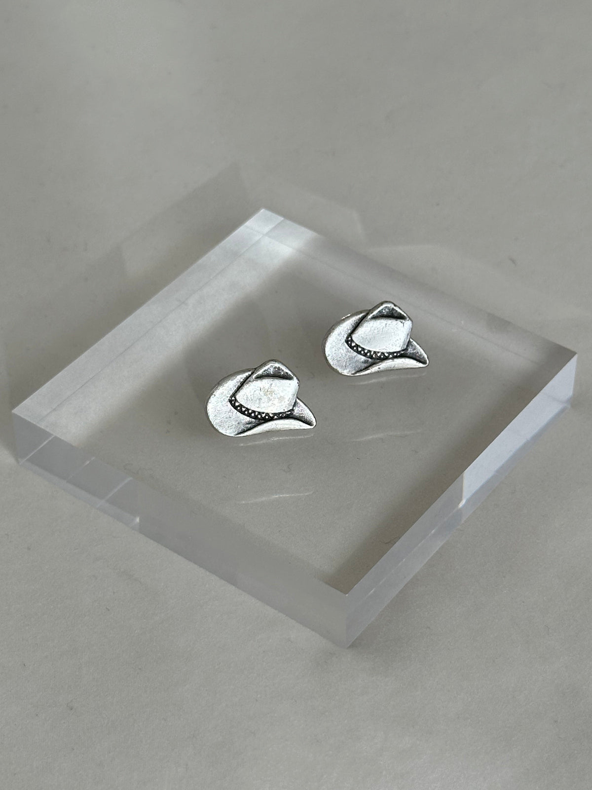 Silver cowboy hat earrings on a clear stand against a gray background