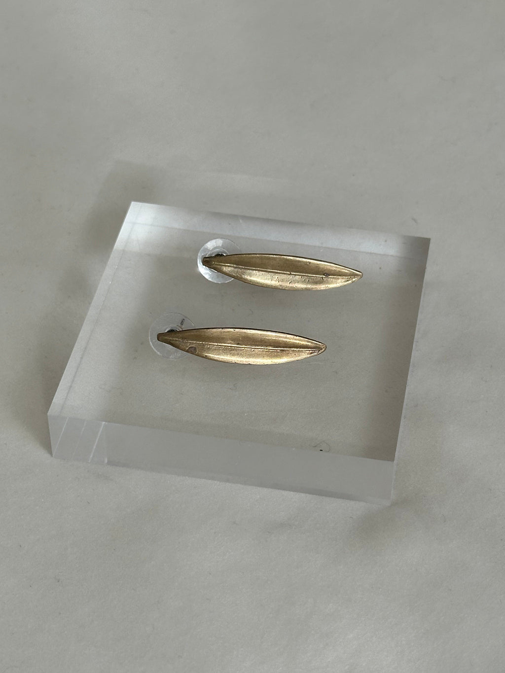 Gold earrings on a clear stand against a gray background