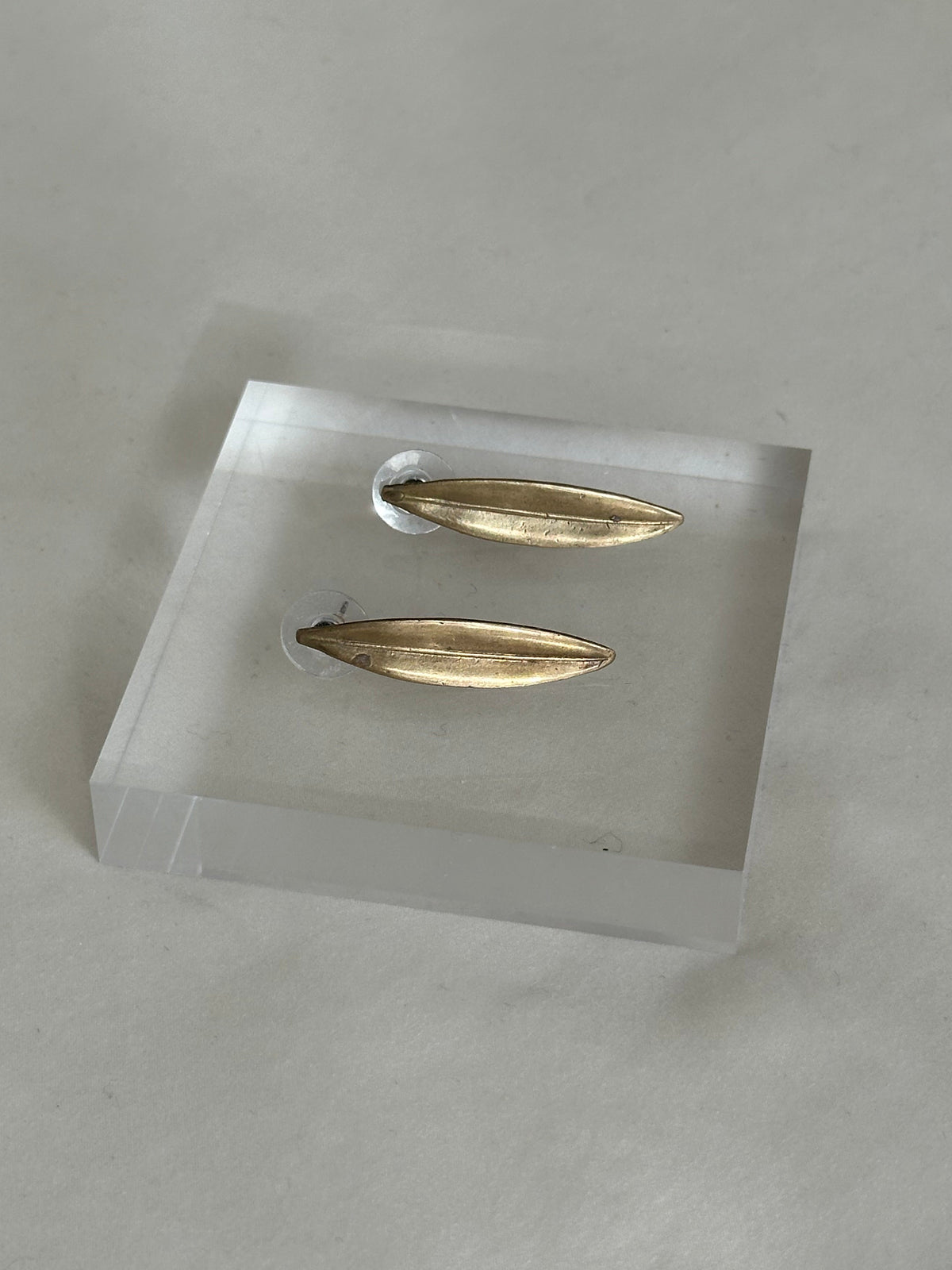 Gold earrings on a clear stand against a gray background